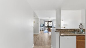 A modern kitchen with a dishwasher, a dining area with a chair, and a hallway leading to a living room.