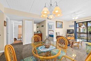 Cozy living area with a dining table for four, wicker chairs, and a large window offering a view of the outdoors.