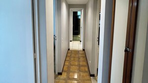 Un pasillo con piso de baldosas, paredes blancas y puertas de madera.