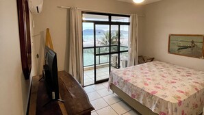 Habitación de hotel con cama, escritorio, televisor, ventilador de techo y un amplio ventanal con vista a la playa.