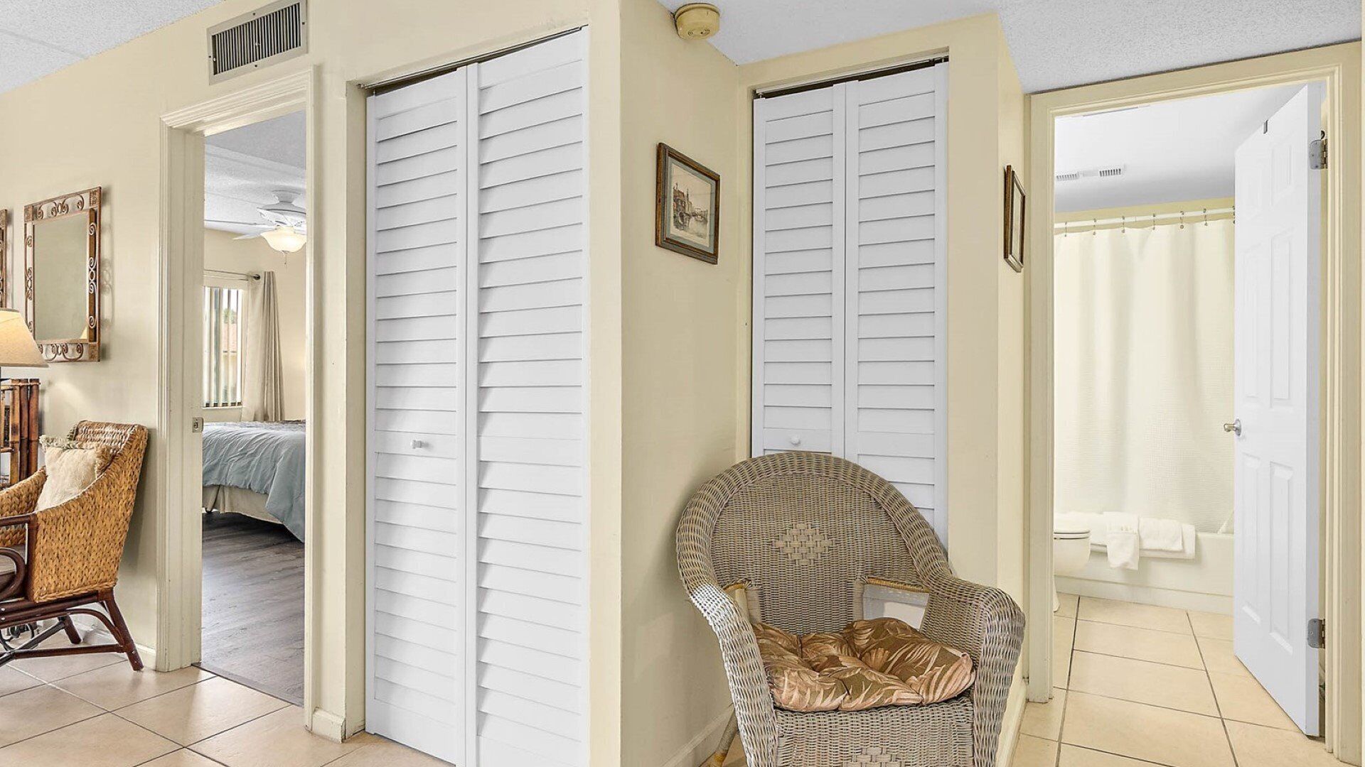 Una habitación con una cama, una silla de mimbre y una puerta que da a un baño.