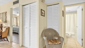A room with a bed, a wicker chair, and a door leading to a bathroom. - Beach Retreat – 2BR/2BA Poolside Condo in Oceanfront Resort, Sleeps 6 (St. Augustine)