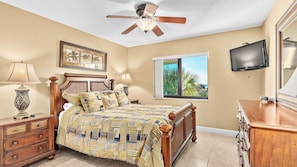 Un dormitorio con cama, ventilador de techo, ventana con vistas, televisor y cómoda.