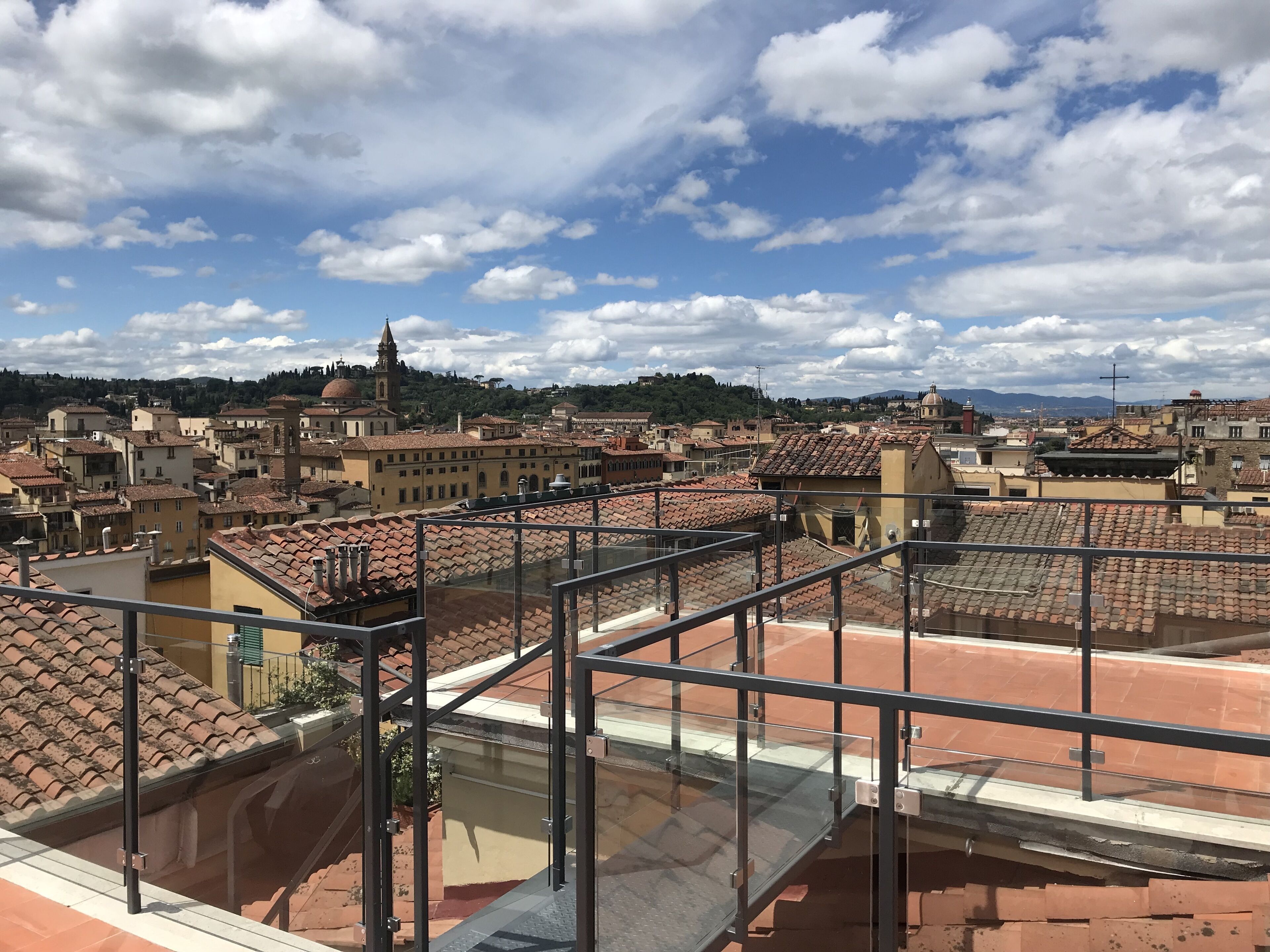 Un paysage urbain avec des bâtiments aux toits de tuiles rouges, un clocher d’église imposant et un ciel dégagé parsemé de quelques nuages.