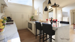 Una cocina moderna con armarios blancos, una isla de mármol y taburetes negros.