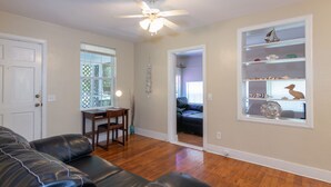 A living room with a leather couch, a dining table with chairs, a ceiling fan, and a bookshelf with decorative items. - Seabird Shack: Dog Friendly, Downtown Pensacola! (Pensacola)