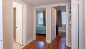 A hallway with wooden flooring, white walls, and a bed in the adjacent room. - Seabird Shack: Dog Friendly, Downtown Pensacola! (Pensacola)