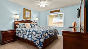 A bedroom with a bed, nightstands, a dresser, a ceiling fan, a window with blinds, and a framed picture on the wall.