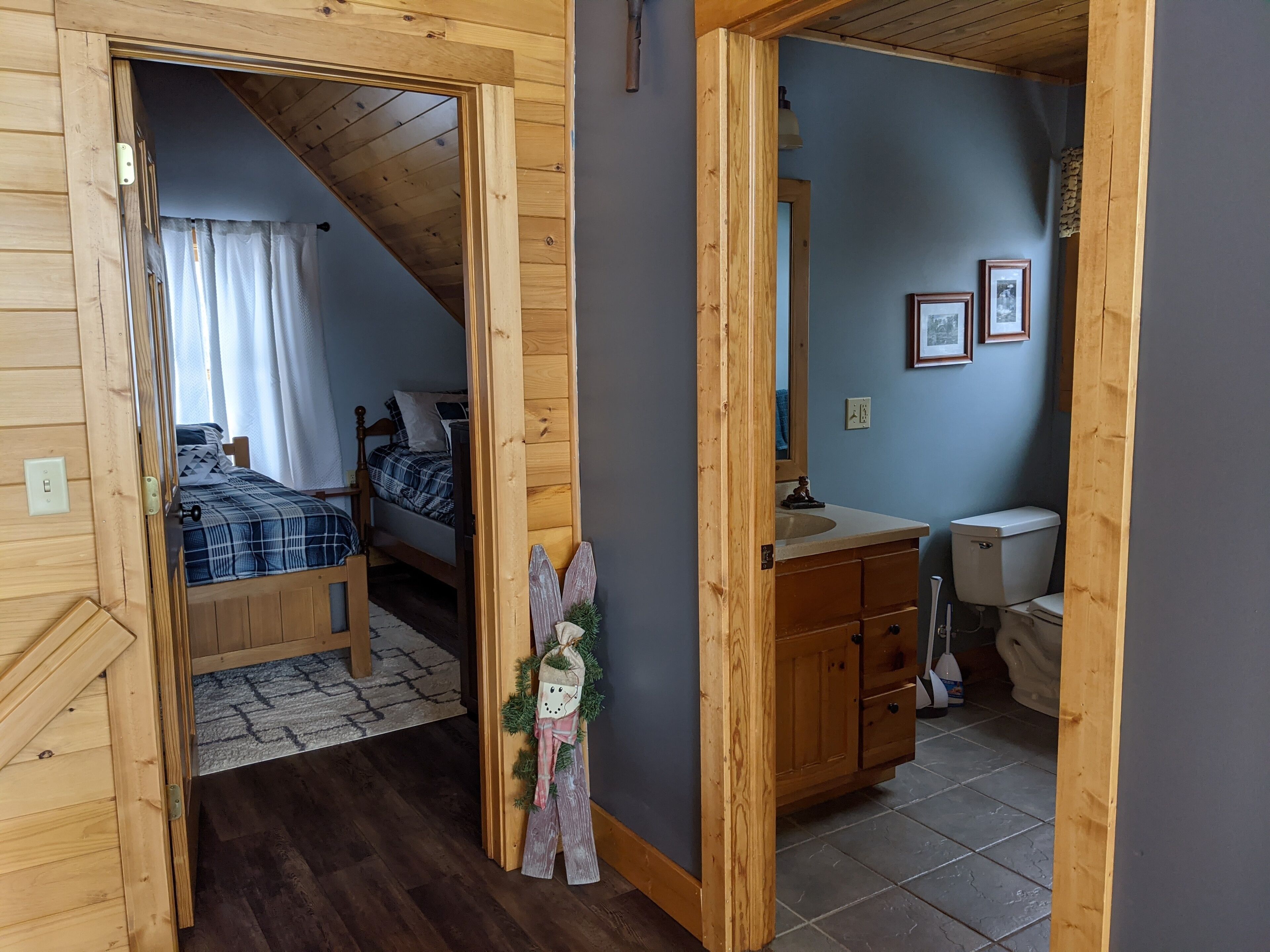 Une chambre avec un lit, une salle de bain avec des toilettes et un couloir avec des murs en bois et un miroir.