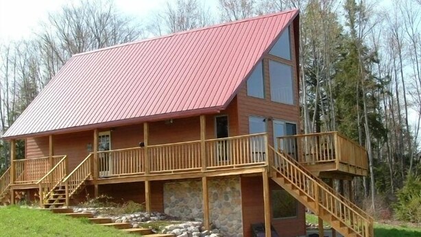Een chalet met twee verdiepingen, een rood dak, houten balkons en een stenen fundering.