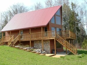 Une cabane à deux étages avec un toit rouge, des balcons en bois et des fondations en pierre.