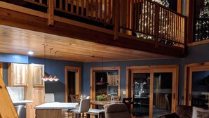 Een ruime woonkamer met een grote bruine bank, een eettafel met stoelen en een keuken met houten kasten en een inbouwoven.