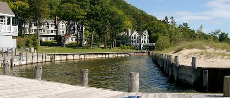 A wooden dock leading to a calm water body, surrounded by lush greenery and residential buildings.