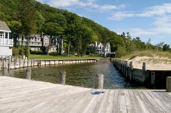 A wooden dock leading to a calm water body, surrounded by lush greenery and residential buildings.