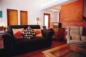 A living room with a sofa, armchair, and a television on a wooden cabinet. - Vintage Beach and Golf Villa (Costa da Caparica)