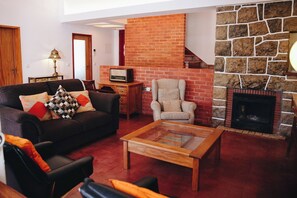 A living room with a sofa, armchair, coffee table, fireplace, and a television. - Vintage Beach and Golf Villa (Costa da Caparica)