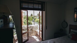 Un dormitorio con cama, mesita de noche, lámpara y vistas a través de una ventana con persianas.