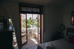 A bedroom with a bed, a nightstand, a lamp, and a view through a window with blinds.