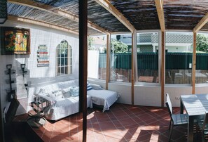 A covered patio area with a cushioned seating arrangement, a dining table, and a view of the surrounding garden. - Vintage Beach and Golf Villa (Costa da Caparica)