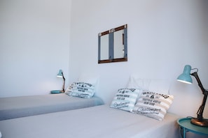 A room with two beds, each with matching pillows and a small table with a lamp. A mirror hangs on the wall above the beds. - Vintage Beach and Golf Villa (Costa da Caparica)