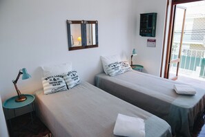 A room with two beds, a wall-mounted mirror, a small table with a lamp, and a window with a view. - Vintage Beach and Golf Villa (Costa da Caparica)