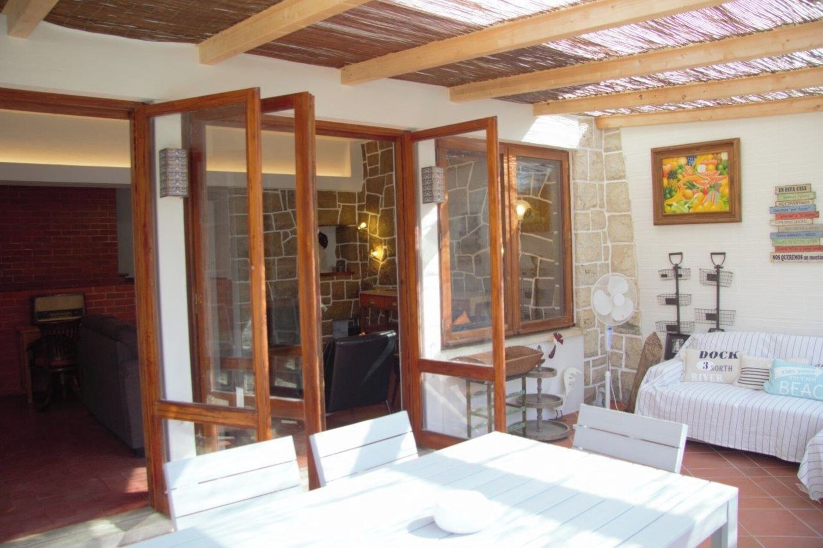 A room with a stone wall, a wooden ceiling, a white sofa, and a table with chairs.