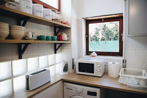 A kitchen with a window, a microwave, a toaster, and a washing machine. - Vintage Beach and Golf Villa (Costa da Caparica)