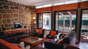 Un salón con pared de piedra, televisor, mesa de centro y asientos, incluyendo un sofá y sillas.