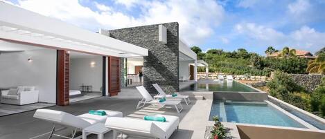 Un espace piscine extérieur moderne, doté de chaises longues et d’un mur en pierre.