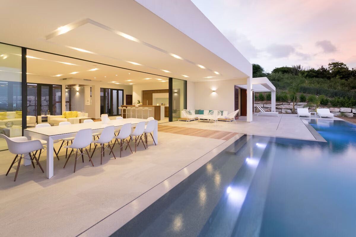 Ein modernes Haus mit Pool, Essbereich und einer Terrasse mit Liegestühlen.