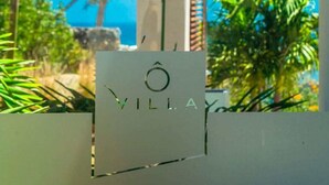 Segno con la scritta 'VILLA' in un font moderno, sullo sfondo di una vegetazione rigogliosa e un cielo azzurro intenso.