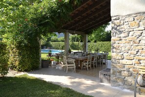 An outdoor patio with a stone wall, wooden pergola, and a pool in the background. - Italian villa, private pool - cycling, hiking, wine tours, slow-food, fast WiFi (Bubbio)