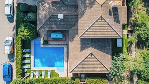 Oversigtsbillede af en boligejendom med swimmingpool, flere biler parkeret langs vejen og en velholdt have.