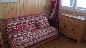 Ein gemütliches Zimmer mit Holzwand, einem Bett mit gemusterten Betttextilien, einem Holzschrank und einem Fenster mit Vorhängen.