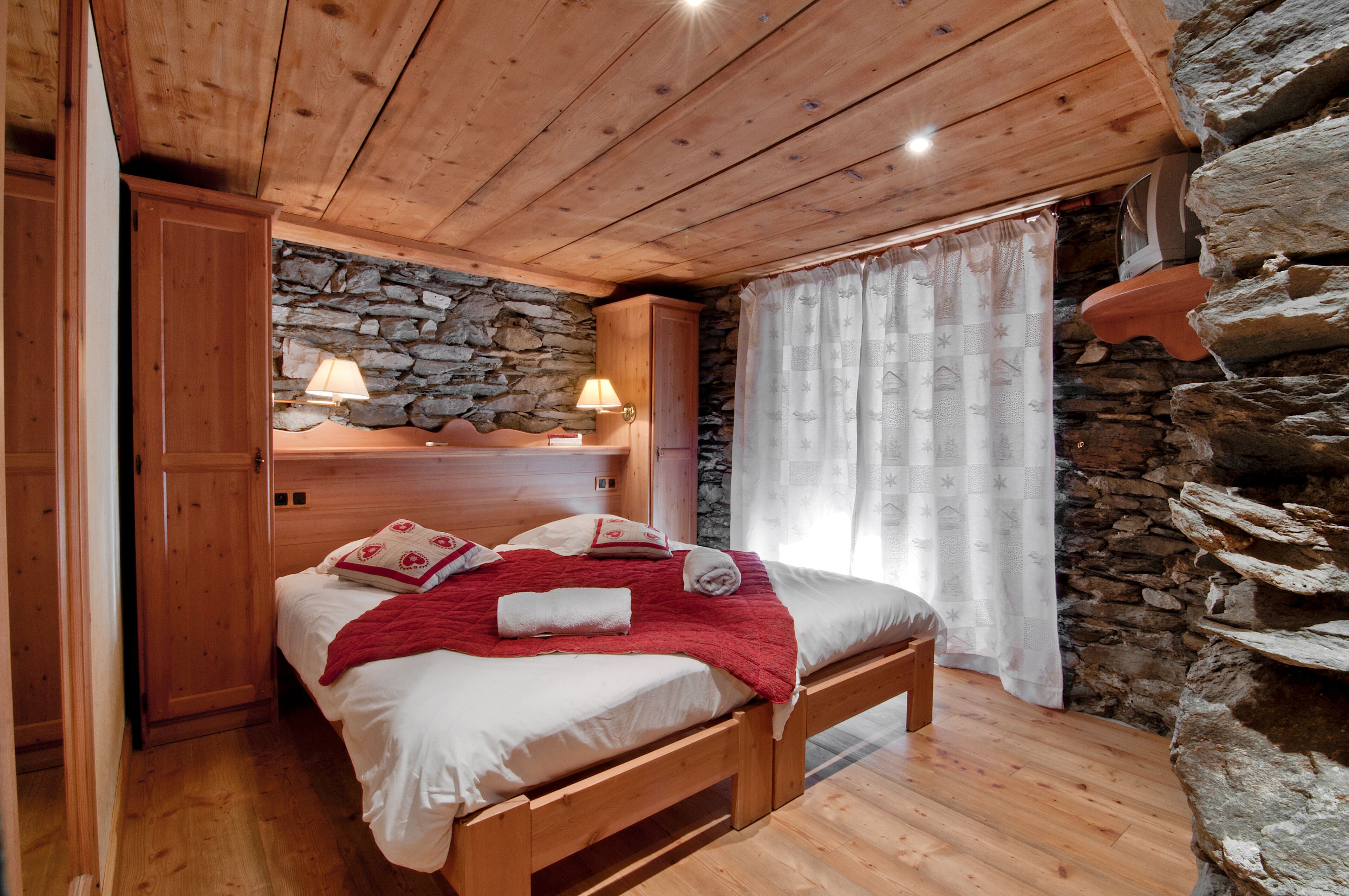 A wooden-framed bed with a stone wall backdrop, a wooden wardrobe, and a stone shelf.