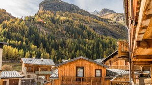 Eine Holzhütte mit Balkon, umgeben von bewaldeten Bergen und einem markanten Gipfel im Hintergrund.