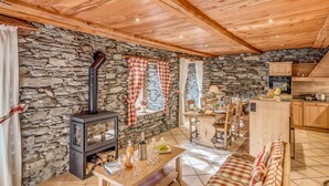 Ein gemütliches Wohnzimmer mit Steinwand, Holzboden, Kamin, Essbereich und Küche.