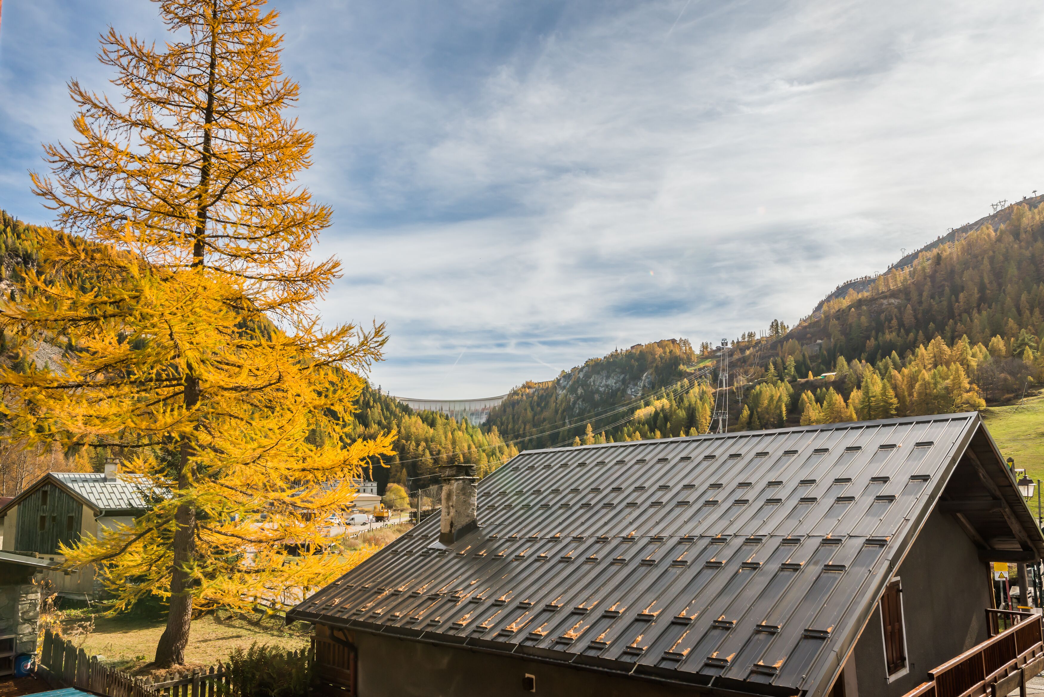 A mountain cabin with a sloped roof, surrounded by autumn foliage and a view of a valley.