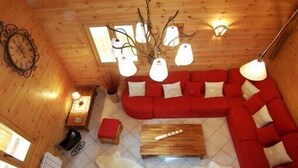 A cozy cabin interior with a red sofa, wooden coffee table, and a fur rug. - Luxury chalet in the Savoie, typical of the Beaufortain area -classified 4 (Villard-sur-Doron)