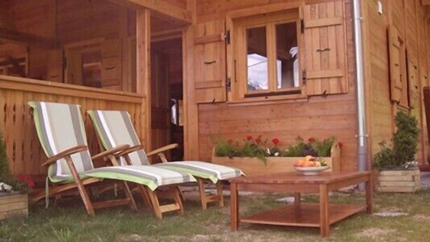 A wooden cabin with two lounge chairs, a table with a fruit bowl, and a window with shutters. - Luxury chalet in the Savoie, typical of the Beaufortain area -classified 4 (Villard-sur-Doron)