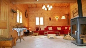 A cozy log cabin interior with a red sofa, a small table, a fireplace, and a wooden ceiling. - Luxury chalet in the Savoie, typical of the Beaufortain area -classified 4 (Villard-sur-Doron)