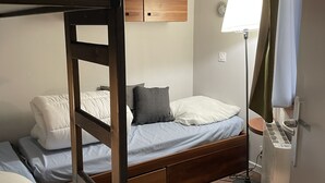 Un dormitorio con literas, un armario de madera, una mesita de noche y una lámpara de pie.
