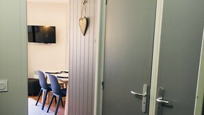 Un pasillo con suelo de madera que conduce a una habitación con una puerta gris, un televisor montado y una decoración con forma de corazón en la pared.