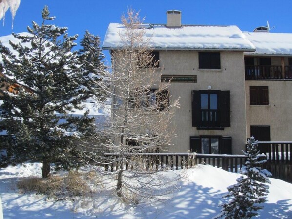 A building with multiple windows and balconies, surrounded by snow-covered trees. - LARGE chalet with garden in Molines-en-Queyras, sleeps 19, fully equipped. (Molines-En-Queyras)