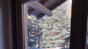 A view through a window of a snowy outdoor area with a wooden deck and a building in the background. - LARGE chalet with garden in Molines-en-Queyras, sleeps 19, fully equipped. (Molines-En-Queyras)