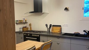 A modern kitchen with a wooden table, a gas stove, and a built-in oven. There are two chairs and a hanging light fixture above the counter. - LARGE chalet with garden in Molines-en-Queyras, sleeps 19, fully equipped. (Molines-En-Queyras)