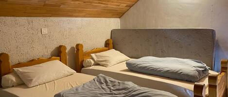 A room with two wooden bunk beds, a textured wall, and a sloped ceiling with a light fixture.