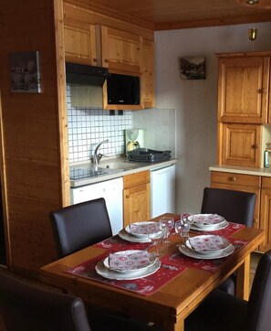Une table de salle à manger en bois, mise avec des assiettes et des verres, un four à micro-ondes au-dessus de l’évier et des armoires en bois.