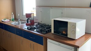 A kitchen with a gas stove, microwave, and a small refrigerator. There is a window with blinds, a sink, and a countertop with various items.