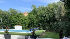 An outdoor seating area with wicker furniture and planters, a pool in the background, and a well-maintained lawn.